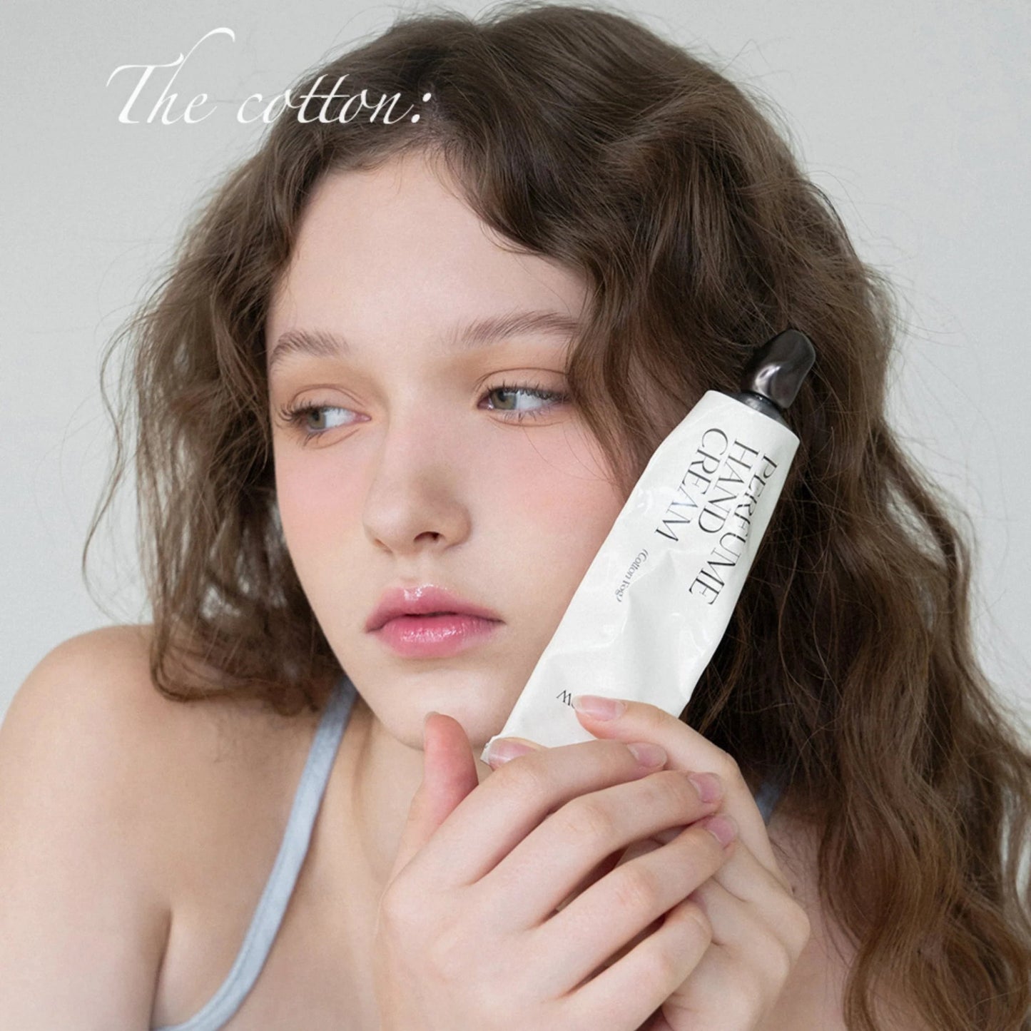 Model holding Afterblow Cotton Fog hand cream near her face.