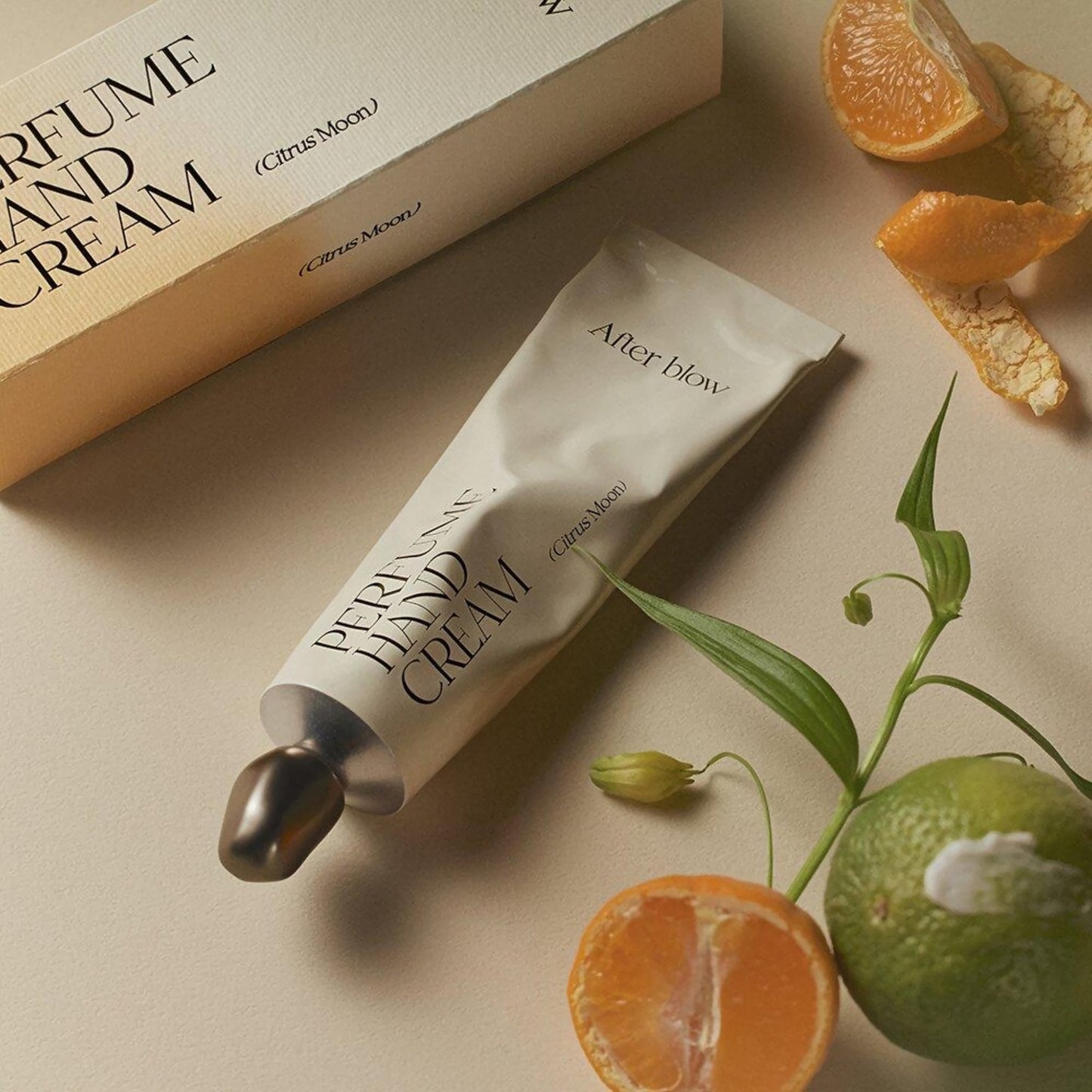 Afterblow Citrus Moon hand cream tube on beige surface with citrus and greenery.