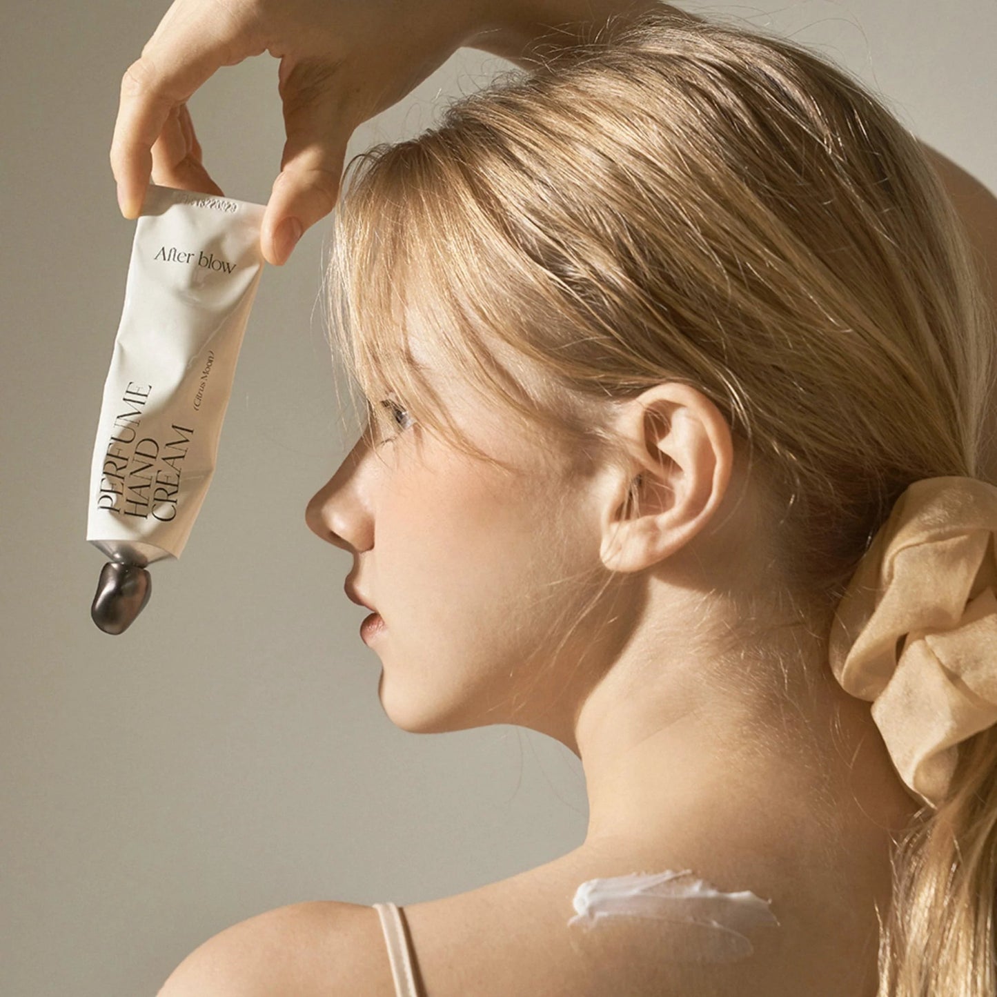 Model holding Afterblow Citrus Moon hand cream next to shoulder with cream swatch visible.