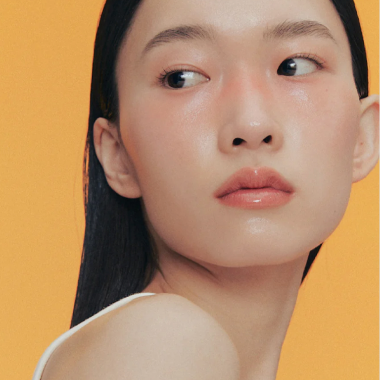 Model wearing Alternative Stereo Aqua Glow with glossy lips and soft peach blush glow.