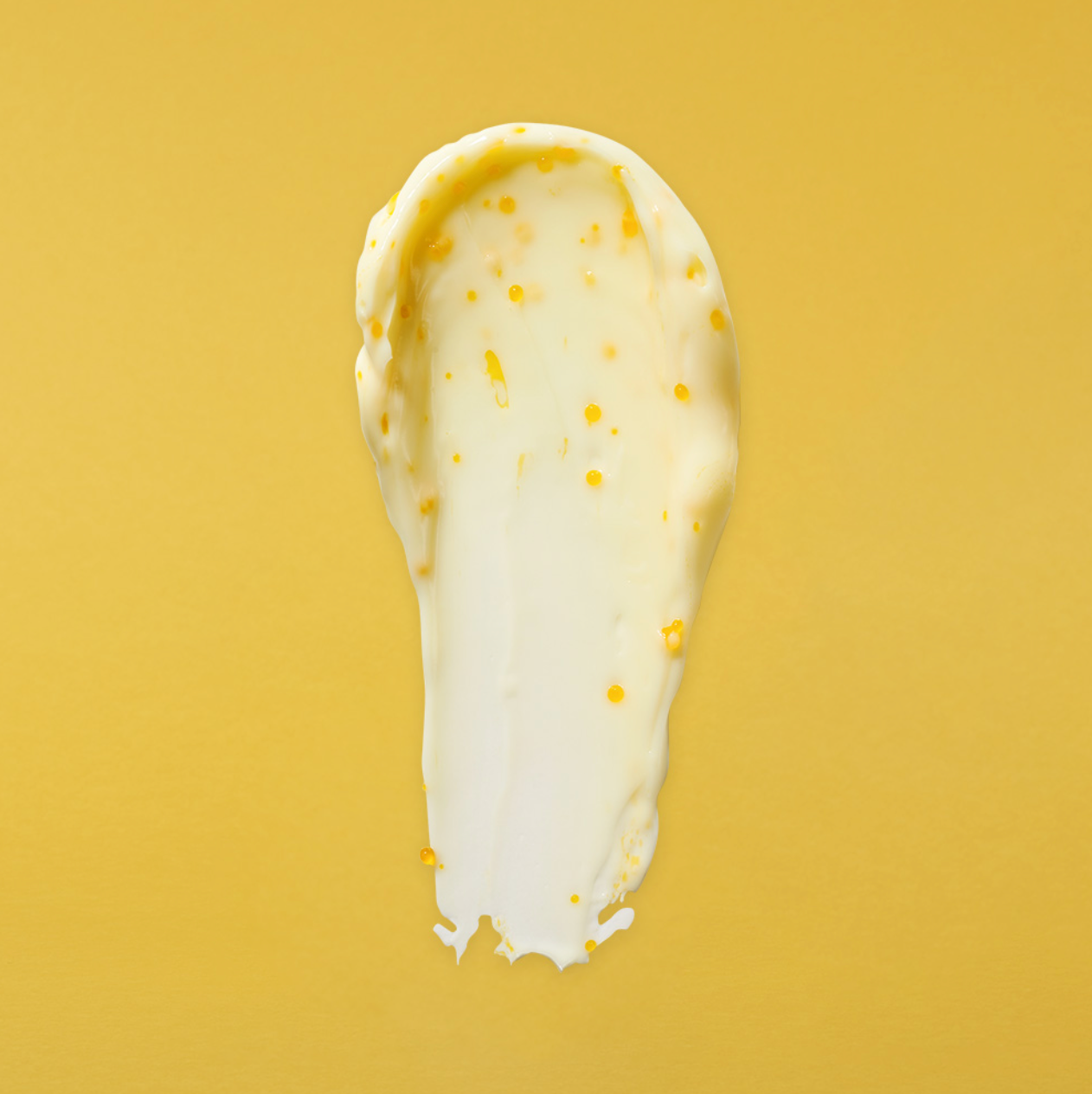 Swatch of Dermafix Vita Collagen Cream with yellow vitamin beads on a yellow background.