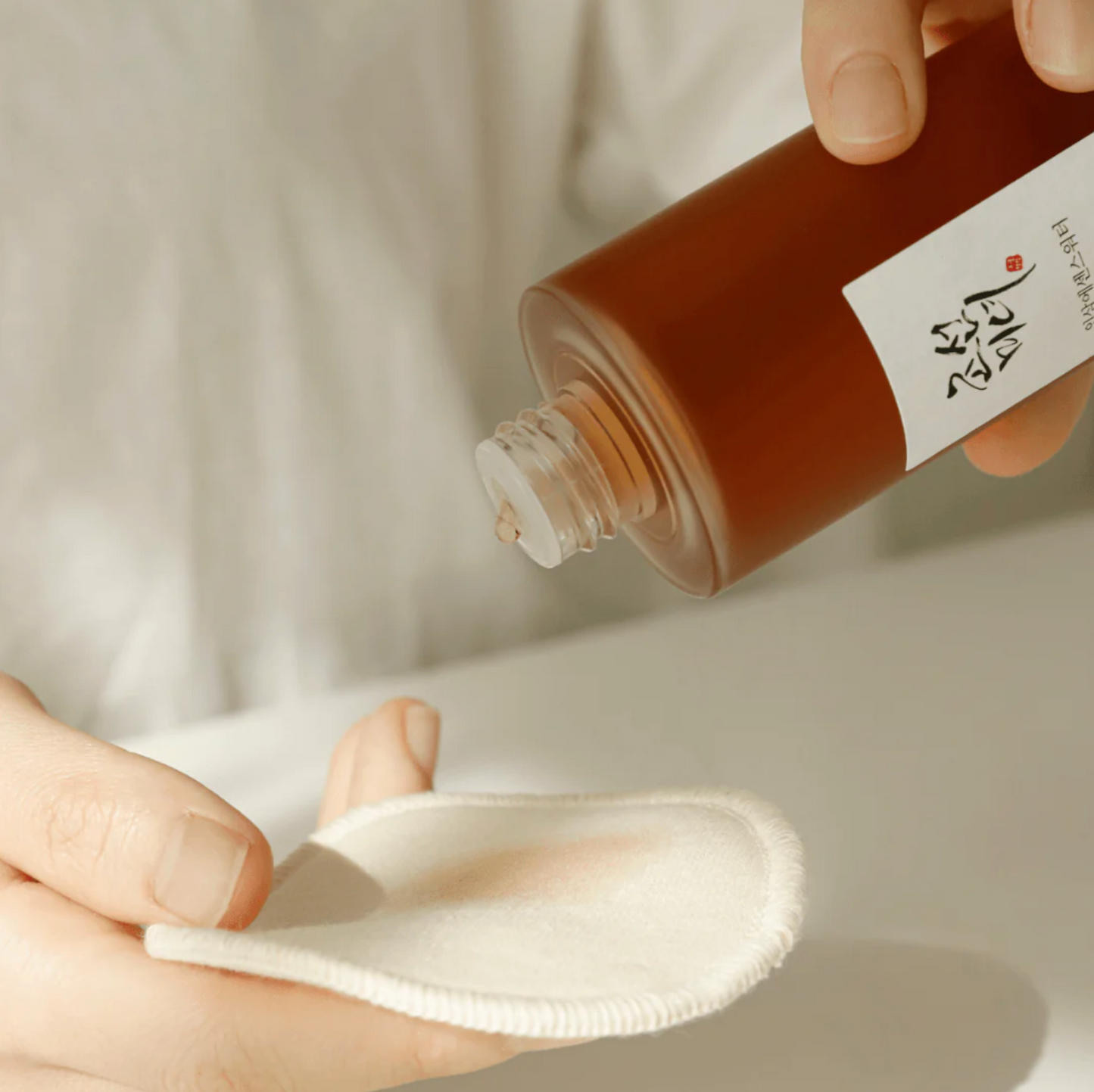 Beauty of Joseon Ginseng Essence Water being poured onto a cotton pad for gentle application.