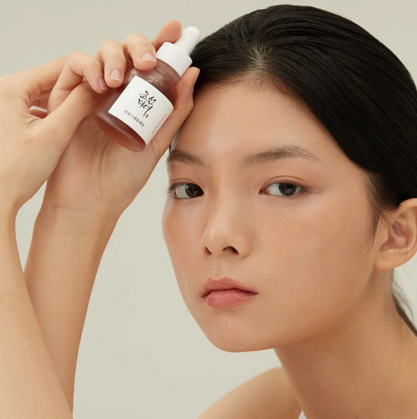 Model holding Beauty of Joseon Revive Serum Ginseng and Snail Mucin near forehead.