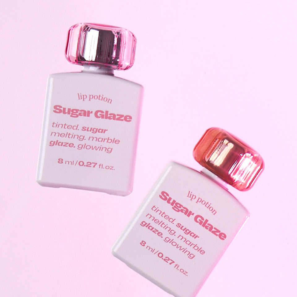 Two bottles of Alternative Stereo Lip Potion Sugar Glaze on pink background – glowing lip tint.