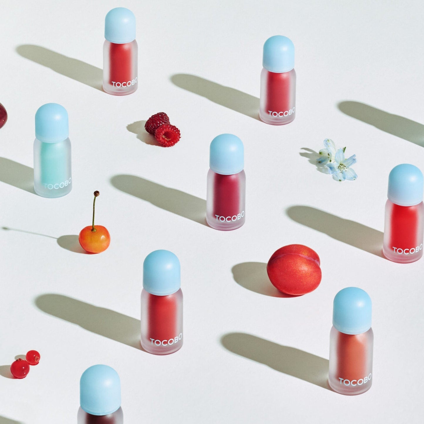 Flatlay of TOCOBO lip oils with fruit and flowers.