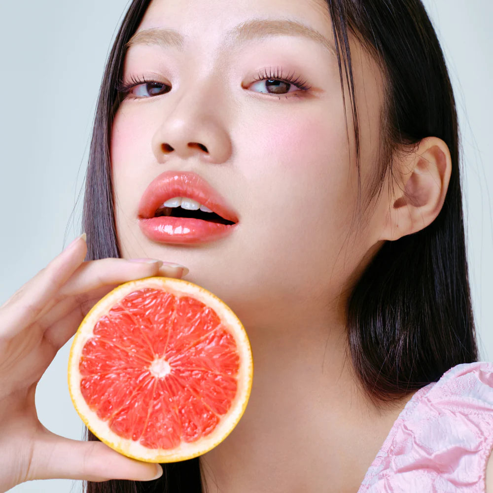 Model holding grapefruit with glossy lips and pink tint.