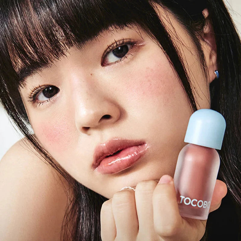 Model holding TOCOBO lip oil with glossy lips.