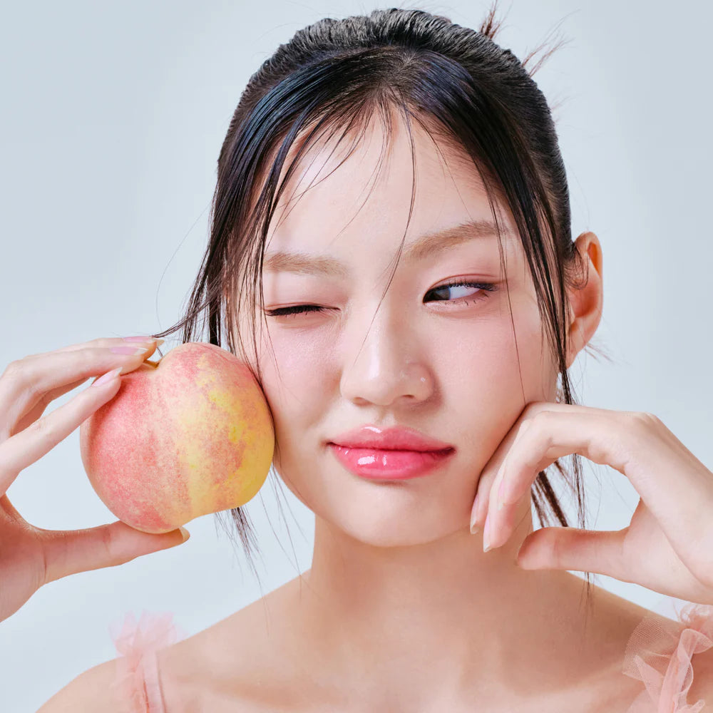 Model holding a peach with glossy lips wearing lip oil.