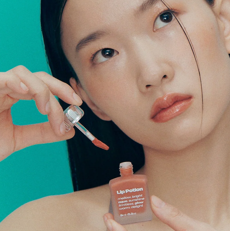 Model using Alternative Stereo Aqua Glow lip tint – soft peach-brown shade with applicator.