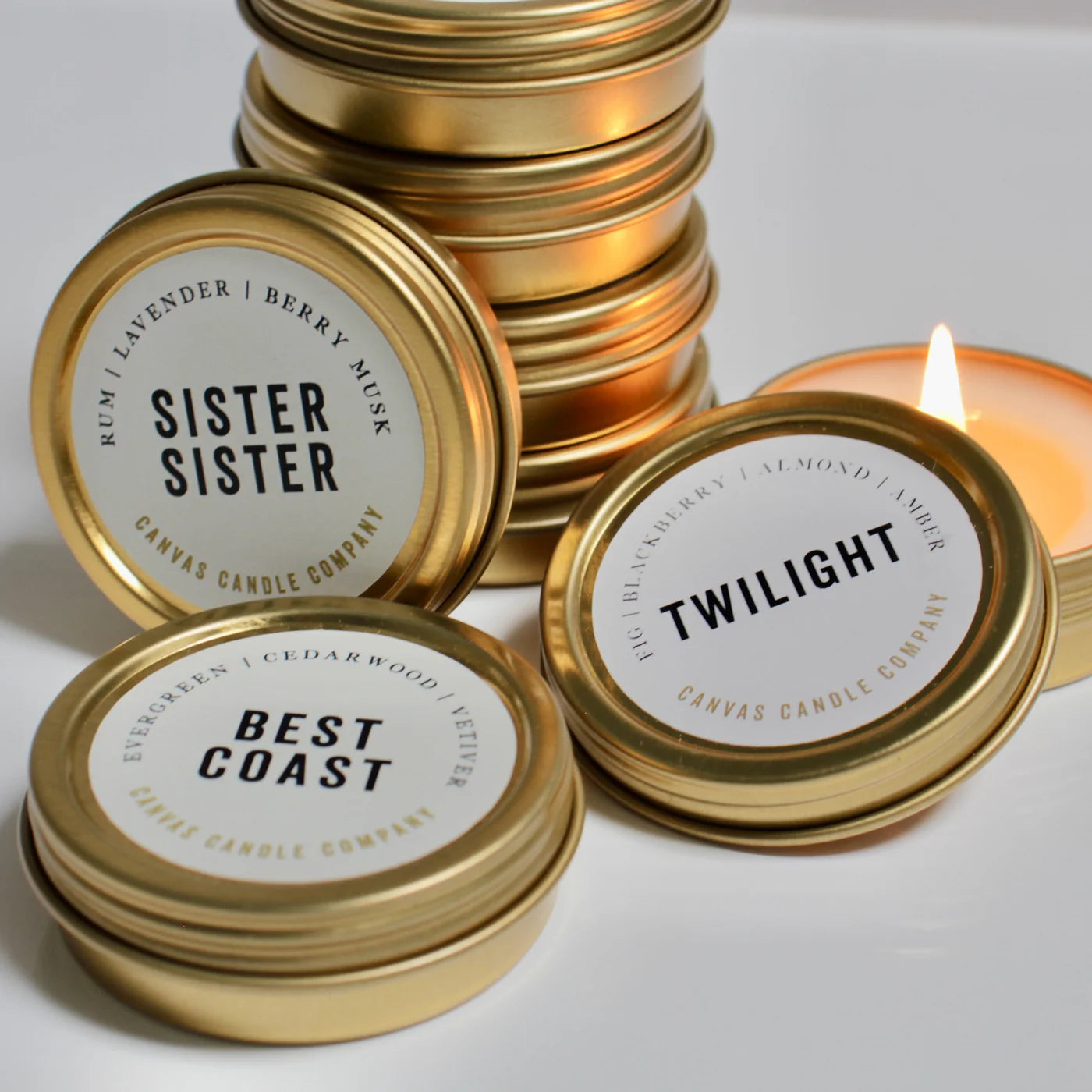 Canvas Candle tins with Sister Sister, Twilight, and Best Coast scents, one lit candle in background.