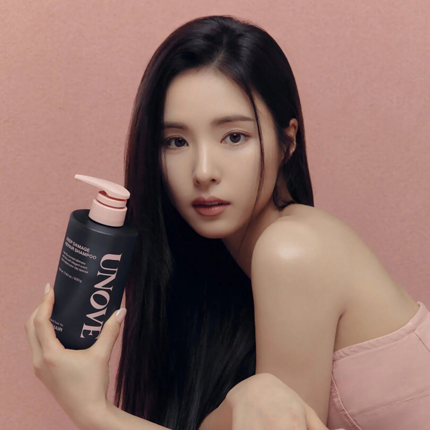 Model with long hair holding UNOVE Deep Damage Repair Shampoo bottle.